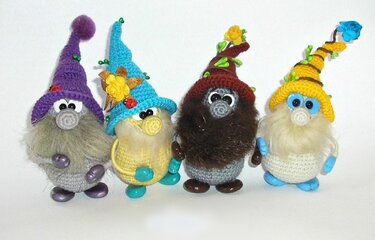 Vier Amigurumi‑Zwerge nebeneinander mit Mützen in Lila, Blau, Braun und Gelb und langen Bärten