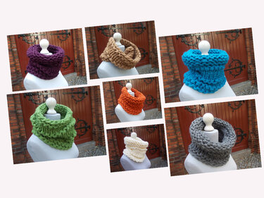 Sechs gestrickte Loopschals in Lila, Grün, Grau, Türkis, Orange und Braun auf Schaufensterpuppen vor einer Holztür
