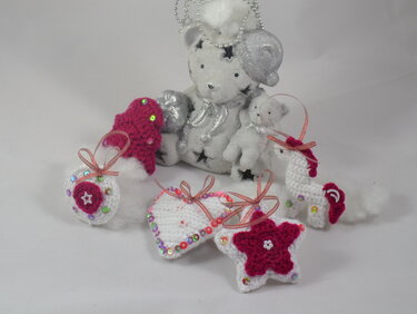 Mehrere kleine gehäkelte Anhänger in Weiß und Magenta: Einhorn, Stern, Herz, Mütze und Kreis, alle mit Pailletten verziert.