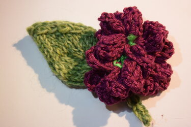 Mehrlagige dunkelviolette gestrickte Blüte mit grünem Blatt, Nahaufnahme