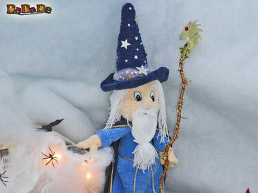 Gehäkelter Zauberer in blauem Gewand mit weißem Bart, sternverziertem Spitzhut und dekorativem Stab vor Halloween-Deko