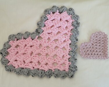 Zwei gehäkelte Herz-Untersetzer: großes rosa Herz mit grauem Rand und kleines hellrosa Herz auf hellem Hintergrund