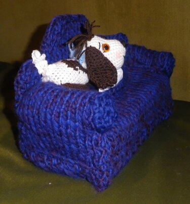 Gestricktes blaues Miniatur-Sofa mit einem kleinen weiß-braunen Amigurumi-Hund darauf