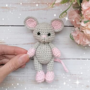 Close-up of small gray crochet mouse with pink details held by hand to show scale