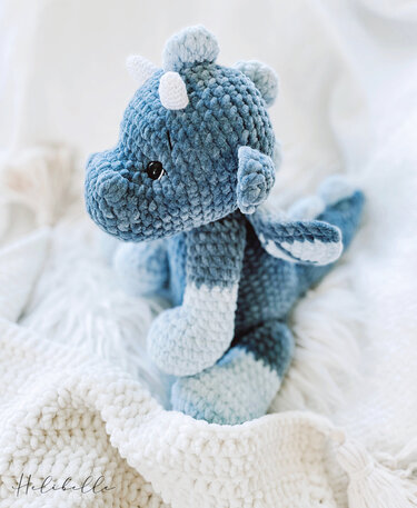 Blauer gehäkelter Amigurumi-Drache mit Hörnern und Flügeln auf weißer Decke