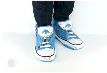 Kinderfüße mit blauen, gehäkelten Sneaker-Hausschuhen mit weißer Zunge