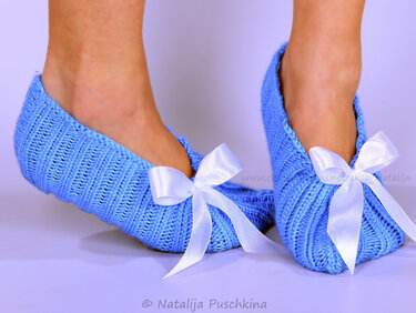 Füße in hellblauen gestrickten Ballerinas mit weißen Satinschleifen