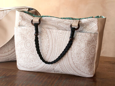 Beige Handtasche mit weißem Mandala-Muster, schwarzen geflochtenen Seilgriffen und hellbraunen Seitenteilen