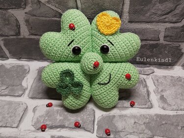 Hellgrünes gehäkeltes vierblättriges Kleeblatt-Amigurumi mit gelbem Herz, Marienkäfern und gestickten Gesichtern