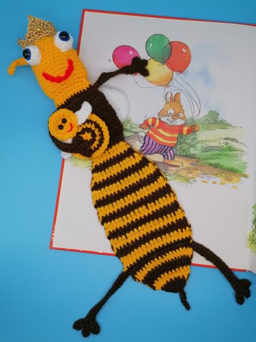 Gehäkeltes Lesezeichen als gestreifte Biene mit Krone in einem geöffneten Kinderbuch.