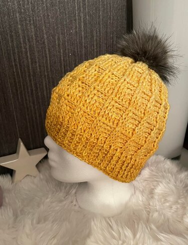 Gelbe Mütze mit Reliefmuster und dunklem Bommel auf weißem Schaufensterkopf