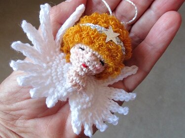 Kleines gehäkeltes Engelchen mit orangefarbenen Locken, Stern-Stirnband und weißen Flügeln in einer Hand