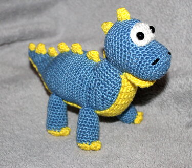 Gehäkelter blauer Amigurumi-Dinosaurier mit gelben Stacheln und großen Augen