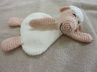 Gehäkeltes Schmusetuch in Schaf‑Form liegend mit cremeweißem Körper und roséfarbenem Kopf und Pfoten