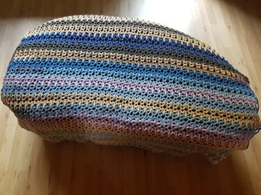 Gehäkelte Decke mit blauen, beigen und pastellfarbenen Streifen auf Holzboden drapiert