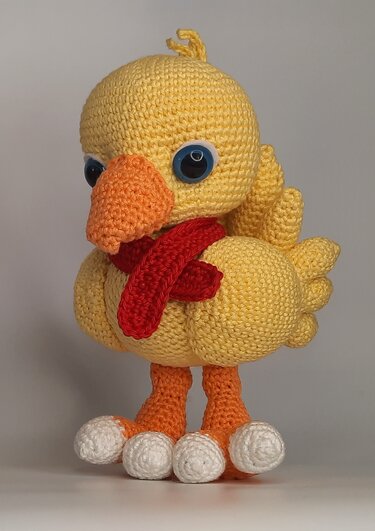 Gelbes gehäkeltes Amigurumi-Küken mit rotem Schal, orangem Schnabel und blauen Augen