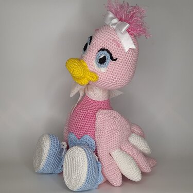 Rosa gehäkeltes Amigurumi-Entchen mit gelbem Schnabel, weißer Schleife, gestickten Augen und blau-weißen Häkelschuhen