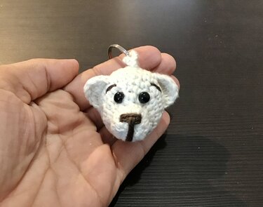 Gehäkelter weißer Teddybärkopf-Schlüsselanhänger in einer Hand