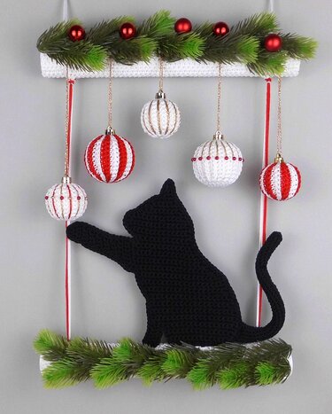Gehäkelte schwarze Katzen-Silhouette mit rot-weißen, verzierten Weihnachtskugeln und Tannengrün