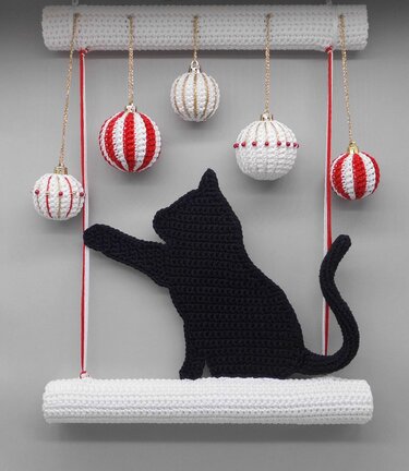 Gehäkelte schwarze Katzen-Silhouette, die nach hängenden rot-weißen und weißen Weihnachtskugeln an einer weißen Häkelstange greift.
