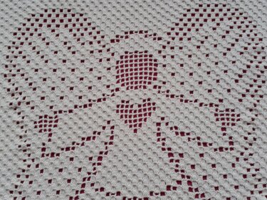 Nahaufnahme des Filet-Häkelmusters einer cremefarbenen Babydecke mit Engel- und Herzmotiv