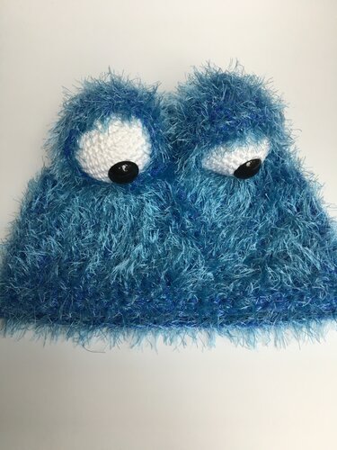 Blaue flauschige gehäkelte Damenmütze mit zwei weißen Augen und schwarzen Knöpfen