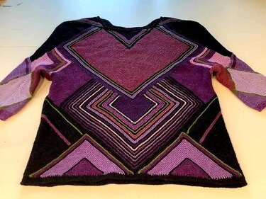 Gestrickte Damen-Tunika in Violett und Schwarz mit geometrischem Muster aus Chevron- und Dreieckselementen und rundem Halsausschnitt.