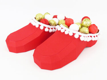 Rote Papierstiefel mit weißem Pomponrand, gefüllt mit goldenen und roten Kugeln