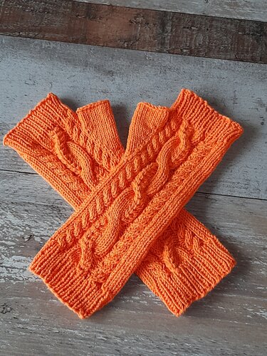 Oranges Paar gestrickter fingerloser Stulpen mit Zopfmuster auf Holzuntergrund