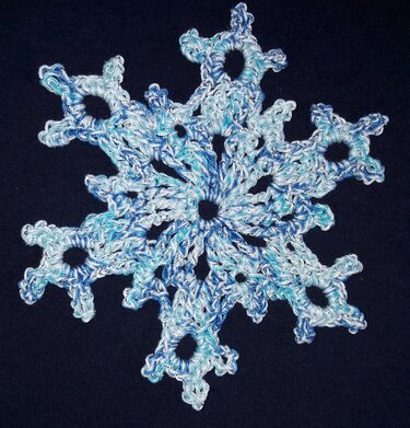 Gehäkelte Schneeflocke in Blau- und Weißtönen auf dunklem Hintergrund