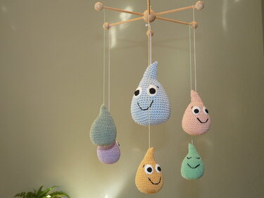 Gehäkeltes Mobile mit fünf bunten Tropfen‑Amigurumis an einem Holzrahmen.