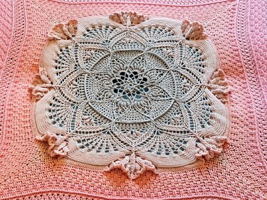 Nahaufnahme einer quadratischen Häkeldecke mit cremefarbenem Mandala auf pastellrosa Grund