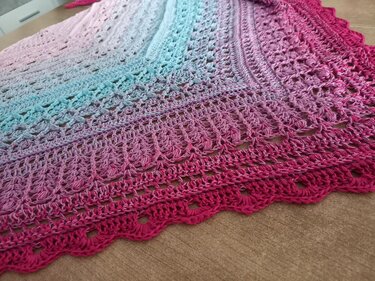 Nahaufnahme eines gehäkelten Dreieckstuchs mit Farbverlauf von Pink zu Türkis, Fokus auf Muschelspitze und Lochmuster