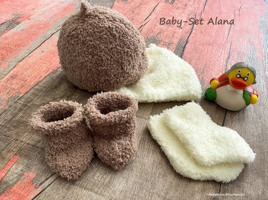 Braunes und cremefarbenes gestricktes Baby-Set mit Mütze, Stiefelchen, Fäustlingen und Quietscheente auf Holzuntergrund