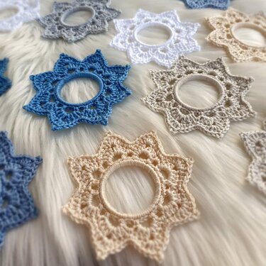 Zarte gehäkelte Sternmotive mit Ringen in Beige, Blau, Grau und Weiß auf hellem Hintergrund
