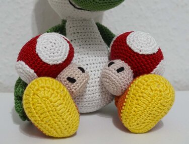 Two red-spotted crochet mushroom amigurumi with yellow soles and beige faces