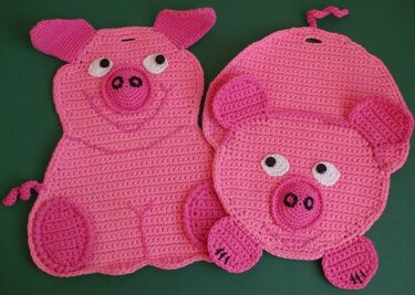 Zwei rosa gehäkelte Topflappen in Schweineform auf grünem Hintergrund