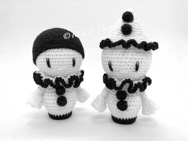 Zwei schwarz-weiß gehäkelte Amigurumi-Figuren mit Rüschenkragen und Knöpfen