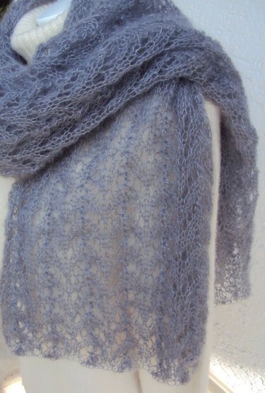 Nahaufnahme eines graublauen, gestrickten Schals mit durchbrochenem Lochmuster aus feinem Garn