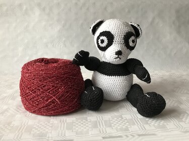 Schwarz-weißer Amigurumi-Panda neben rotem Garnknäuel zur Materialansicht