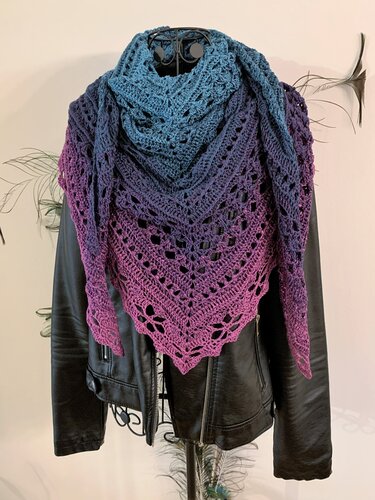 Blue-to-purple ombre crochet triangle shawl with lace pattern, draped over a black leather jacket on a mannequin.