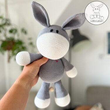 Hand holding a grey and white crocheted amigurumi donkey showing stitches and long ears