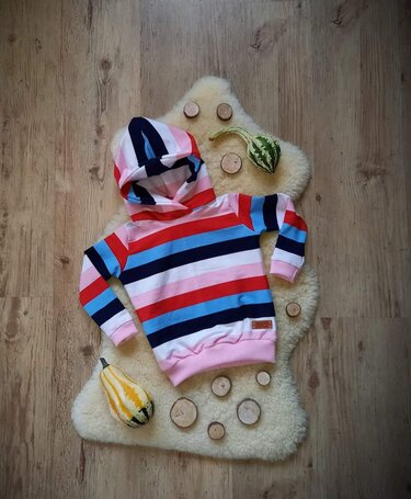 Gestreifter Kinder-Hoodie mit Kapuze auf hellem Fell, umgeben von Holzscheiben und Zierkürbissen