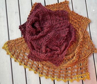 Zwei gehäkelte Dreieckstücher in Burgunderrot und Gelborange mit Lochmuster auf hellem Holz.