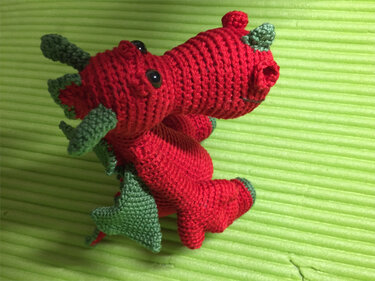 Rot-grüner gehäkelter Amigurumi-Drache mit Flügeln auf grünem Hintergrund