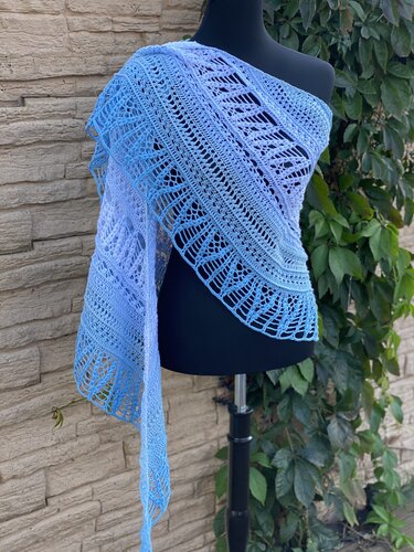 Halbrundtuch in Blau‑Lila Verlauf mit Ajour‑ und Fächermuster auf schwarzer Schneiderpuppe vor Steinmauer