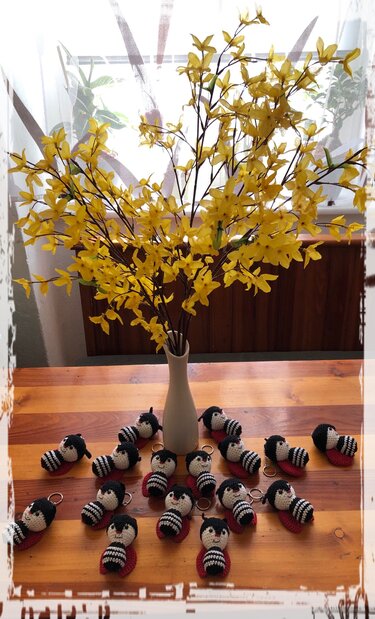 Gehäkelte Marienkäfer-Schlüsselanhänger auf Holztisch, umgeben von gelben Blütenzweigen in Vase