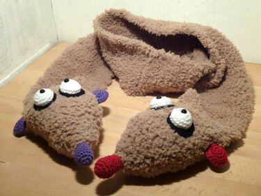 Flauschiger hellbrauner Häkelschal mit weißen Kulleraugen und bunten Applikationen an den Enden