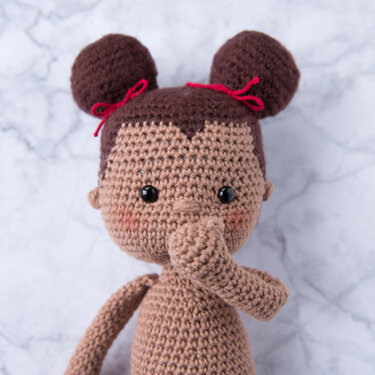 Gehäkelte Amigurumi-Puppe mit zwei Dutts, roten Schleifen und Hand am Mund