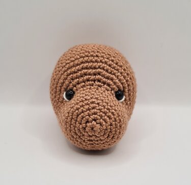 Detailaufnahme eines braunen gehäkelten Amigurumi-Kopfs mit sichtbaren Maschen und schwarzen Augen